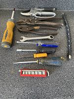 Top view of all assorted hand tools laid out on a dark textured surface, includes screwdrivers, pliers, wrench, socket set and flexible segmented cable guide.