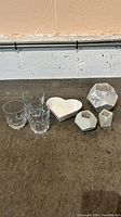 Photo of 3 clear glass cups, 3 marbled geometric mini plant holders, and 1 white heart-shaped ceramic tray placed on a concrete floor.