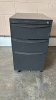 Front view of black metal file cabinet with three drawers and slight visible wear