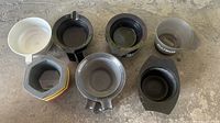 Top view of various plastic bowls including black, white, transparent, and gray, some with handles or spouts, placed on a floor.