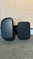 Top view of two black salon chair boosters lying side by side showing seat and backrest shapes