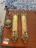 Photo of four items: two matching brass wall candle holders, one brass door knocker, and one small brass vase or candle holder on a wooden surface.