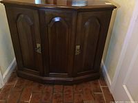 Front view of the dark wood cabinet showing the three-door angled front with metal handles.