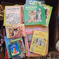 Overview of about 15 cat books stacked and fanned out, showing colorful children's book covers with cats on them including Kittens Are Like That and Curley Cat Baby-Sits.