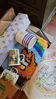 Box containing ceramic mugs, colorful latch-hook cat rug, and some greeting cards with cat themes