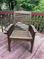 Wooden outdoor patio chair front view on wooden deck showing slatted seat and armrests