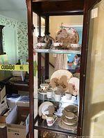 Cabinet shelf with assorted china including plates, cups, saucers, and a teapot visible on three shelves.