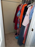 Closet space with various ladies plus size clothing hanging on hangers, showing colorful dresses and tops including a bright orange and burgundy piece