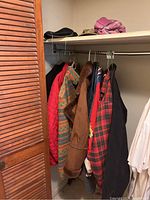 Closet with multiple men's and ladies coats hanging, showing various colors, materials and styles including a brown ultrasuede coat and plaid patterned coats.
