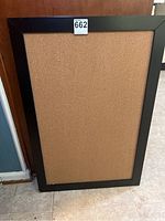 Full view of the rectangular corkboard standing against a wall showing the full cork surface and black frame.