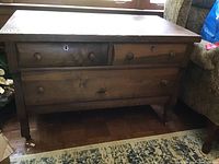 Front view of vintage wooden dresser showing three drawers with round knobs and wheels on legs