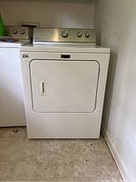 Full front view of the white Maytag dryer showing the door and some part of the room floor and wall.
