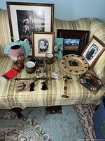 A variety of Indigenous American themed items including framed artwork, pottery, mugs, wooden plaques, figurines, and a decorative plate arranged on a striped sofa.