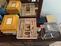 View of gold-tone decorative lidded boxes, jewelry organizer tray with mixed jewelry, and small containers on table