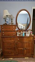 Front view of the large wooden Pulaski Keepsakes dresser with 8 drawers and bottom cabinet, items on top, and oval mirror