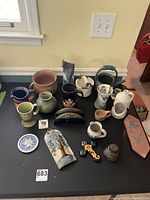Full view of all pottery and decorative items on table showing variety of pitchers, mugs, plaques, and small pots.