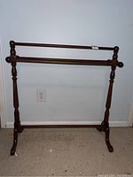 Front view of a wooden quilt rack with turned legs and two horizontal bars for hanging quilts.