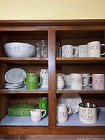 Shelving with Rae Dunn dishware including large white bowl, mugs, plates and glassware
