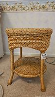Full side view of round rattan two-tier table showing the woven rattan legs and shelf with visible wear.