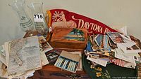 Lot display of vintage postcards, glassware, wooden souvenir box, cocktail forks, and pennant