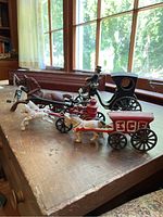 Side view of three metal vintage toys showing horses, wagons and carriage with driver figure