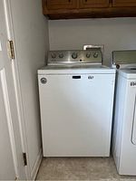 Full frontal view of white Maytag washing machine with partial view of adjacent dryer and laundry area.