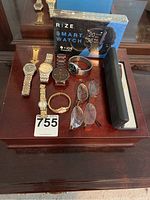 Photo showing multiple wristwatches, boxed Rize smart watch, two pairs of eyeglasses, and a wooden jewelry box on a wooden surface.