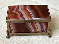 Front and top view of rectangular snuff box showing polished banded agate lid with brass frame and ball feet
