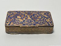 Top view showing blue enamel lid with gold floral vine patterns, rectangular shape with hinge side visible.