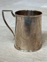 Front view of tapered cylindrical silver mug showing body and handle