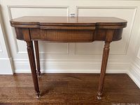 Front view of closed table showing top surface, apron, and four fluted legs with casters