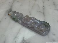 Angled view showing entire pendant lying flat, foo dog head at top and cloud motif below