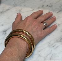 Two gold tone oval bangles stacked on wrist against marble surface