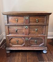 Front view showing three drawers with brass hardware and bun feet