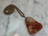 Full view of pendant and chain laid on marble surface