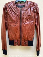 Front view of cognac leather hooded bomber jacket on hanger