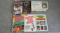 Box of 1991 Donruss baseball cards with handwritten label, three books of baseball card value guides, and two VHS tapes with baseball themes.