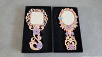 Both decorative hand mirrors placed side by side in presentation boxes on a gray surface