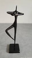 Front view of sleek black slender ballerina sculpture with arms extended and one bent leg on square base