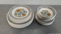 Top view of the three sizes of stacked plates on the left and the bowls stacked on the right showing the Seychelles floral design and size variation.