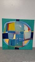 Front view of large abstract unframed canvas painting showing oval geometric design with teal background and various colors