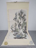 First image shows one vertical scroll partially rolled, depicting mountainous landscape, trees, calligraphy and red seals at the bottom and sides, mounted on beige scroll backing.