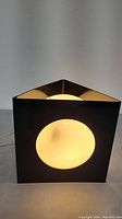 Front view of the black triangular frame lamp with a round white illuminated glass globe inside.