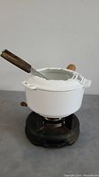 Side angle of white enamel fondue pot with wooden handle and fondue fork inserted