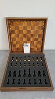 Wooden folding chess board with foam storage insert for chess pieces, showing the top side with alternating wooden squares and decorative border.