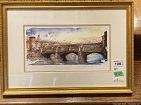 Framed watercolor style print of a bridge and buildings with artist signature, view of full frame and image.