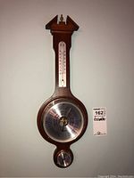 Front view of the wooden Thermor barometer showing the metal circular barometer dial with including pressure and weather information, the vertical thermometer above, and small circular dial at the bottom.
