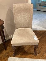 Front and angled view of the beige fabric covered wood frame dining chair showing carved legs and high backrest.