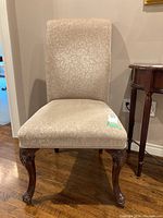 Front view of a beige fabric upholstered wood frame chair with carved legs and floral pattern fabric.