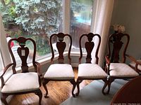 Four wooden dining room chairs arranged in front of window, showing carved backs and light fabric seats.